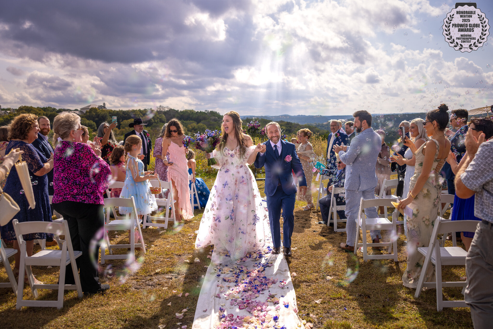 2025 ProWed Global Award Honorable Mention Photo of a bride and groom walking down the aisle after their outdoor wedding ceremony at Wyndham World Mark in the Texas Hill Country under dramatic thunderstorm breaking sunlight
